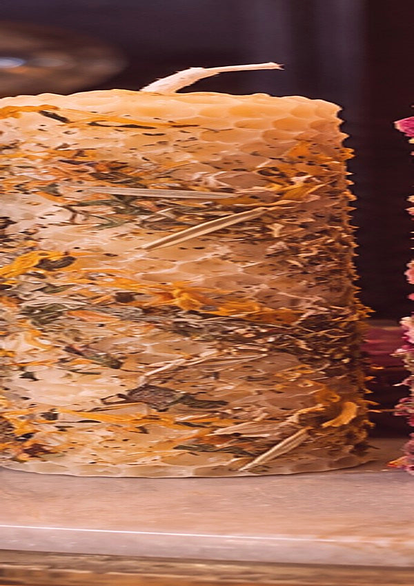 Concept photograph of blush pink rolled beeswax candle with botanicals